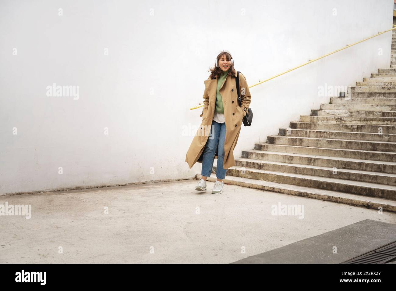 Glückliche Frau mit Mantel, die auf der Treppe nach unten zieht Stockfoto