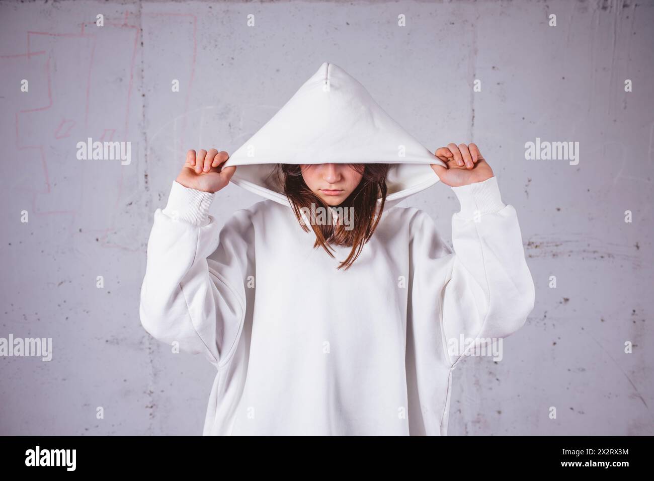 Mädchen mit weißem Hoodie vor grauem Zementhintergrund Stockfoto