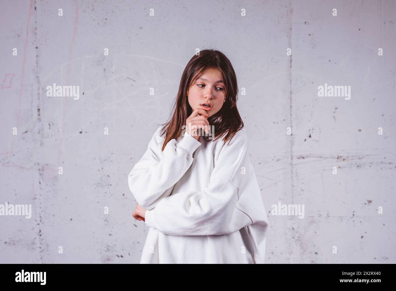 Mädchen in weißem Kapuzenpulli posiert vor grauem Zementhintergrund Stockfoto