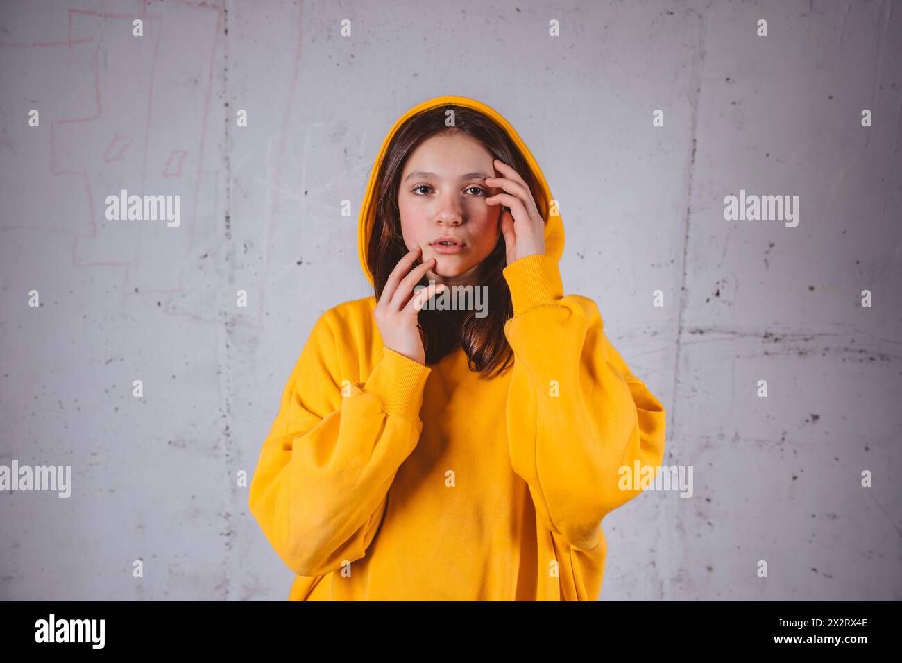 Mädchen in gelbem Kapuzenpulli posiert vor grauem Hintergrund Stockfoto