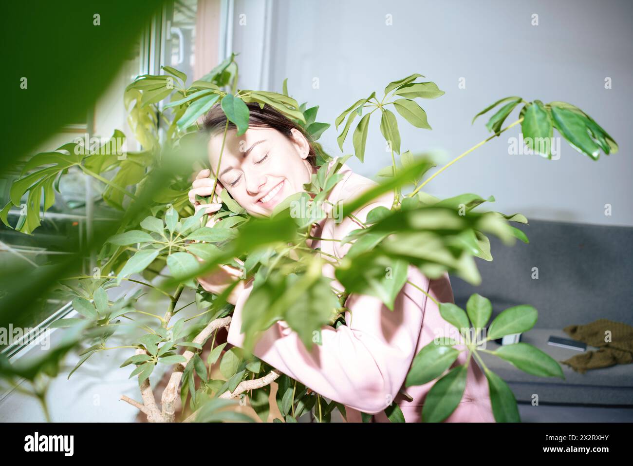 Lächelnde Geschäftsfrau mit geschlossenen Augen inmitten grüner Pflanzen zu Hause Stockfoto