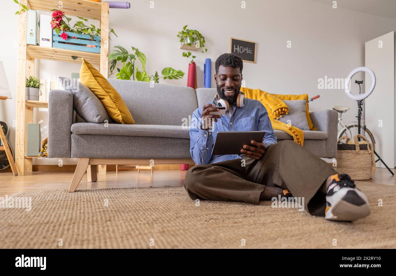 Glückliche, nicht binäre Person, die zu Hause auf einem Tablet-PC per Kreditkarte bezahlt Stockfoto