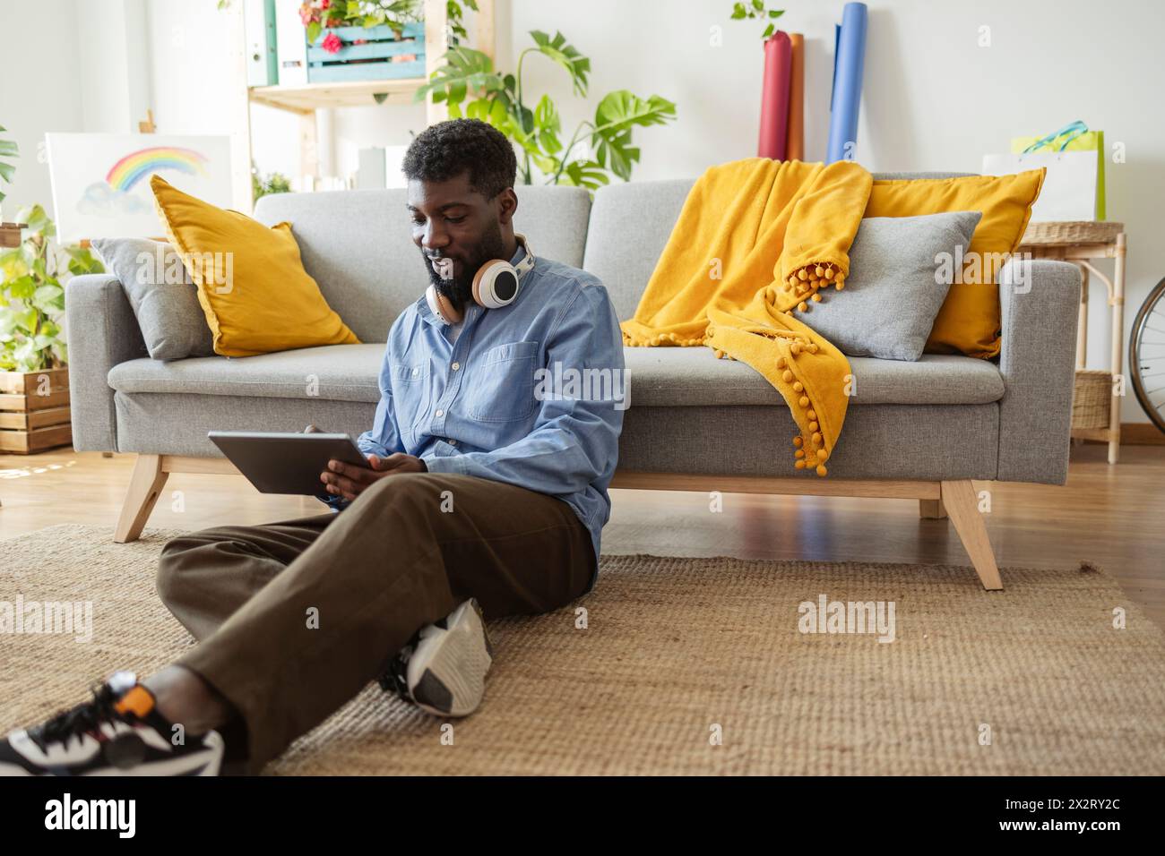 Lächelnde, nicht binäre Person, die zu Hause einen Tablet-PC verwendet Stockfoto