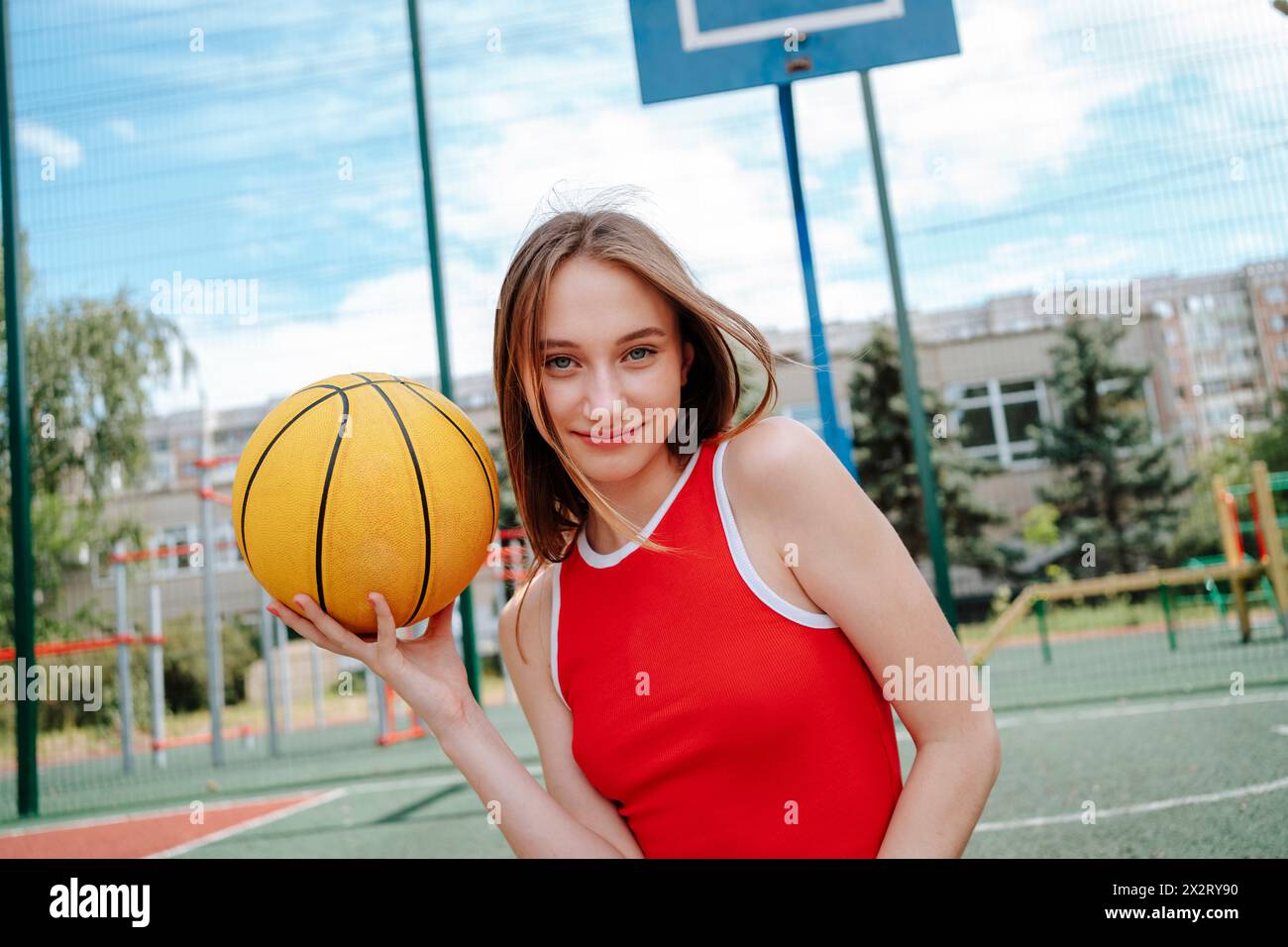 Lächelnder Basketballspieler mit Ball auf dem Schulhof Stockfoto