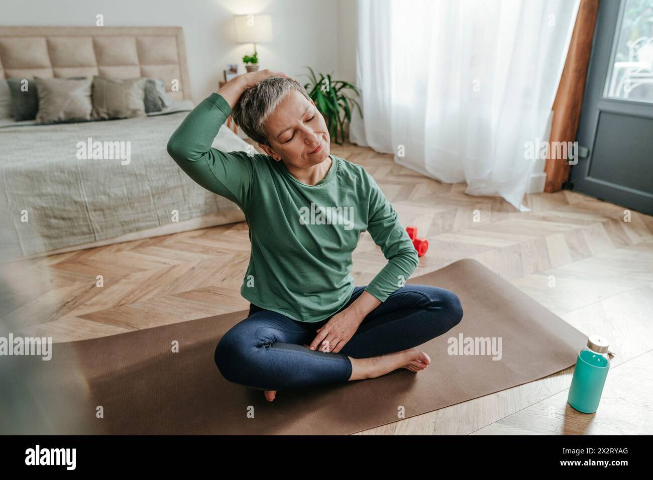 Frau, die den Kopf dehnt und zu Hause auf Yogamatte sitzt Stockfoto