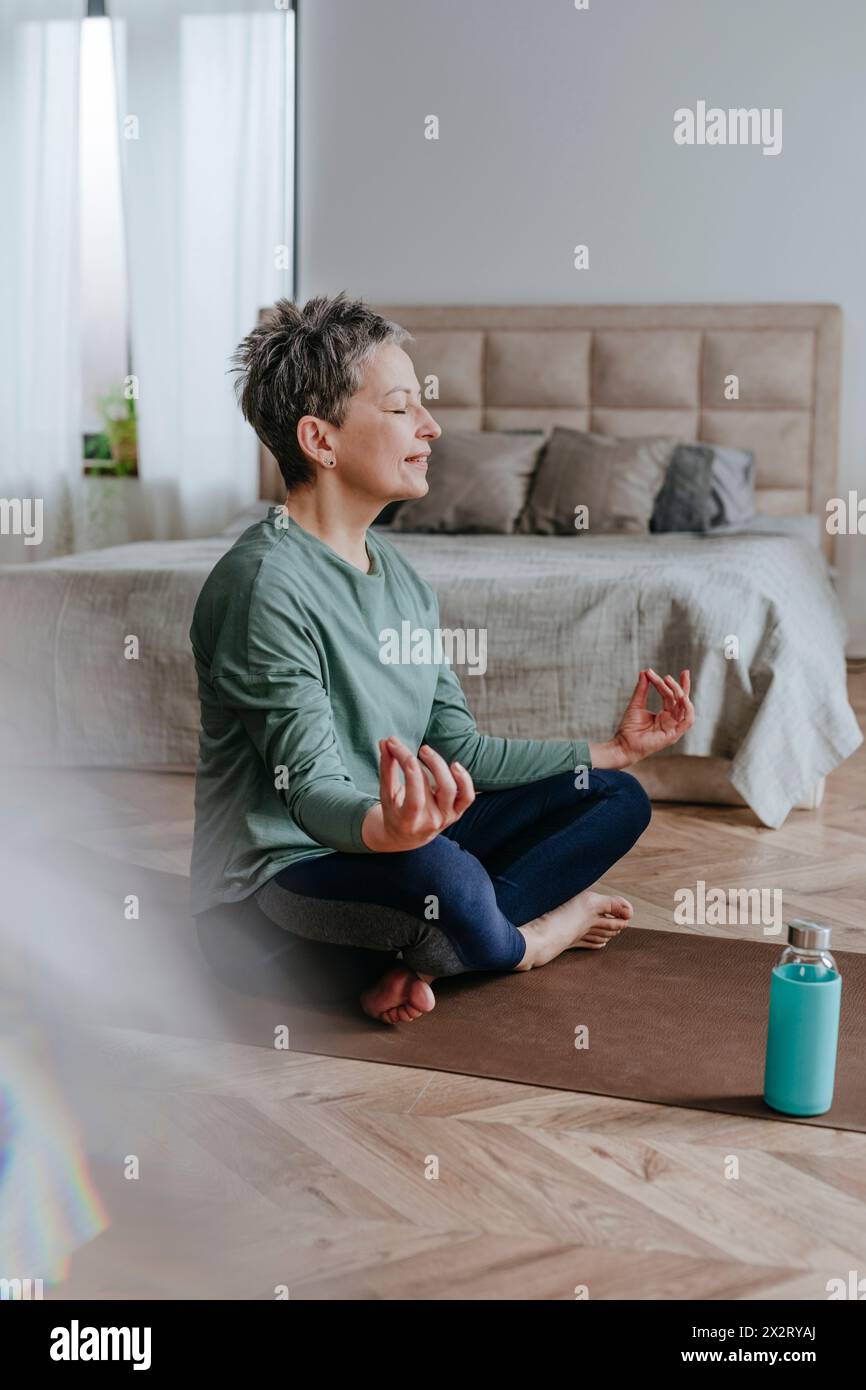 Lächelnde Frau, die zu Hause mit Kreuzbeinen auf Yogamatte meditiert Stockfoto