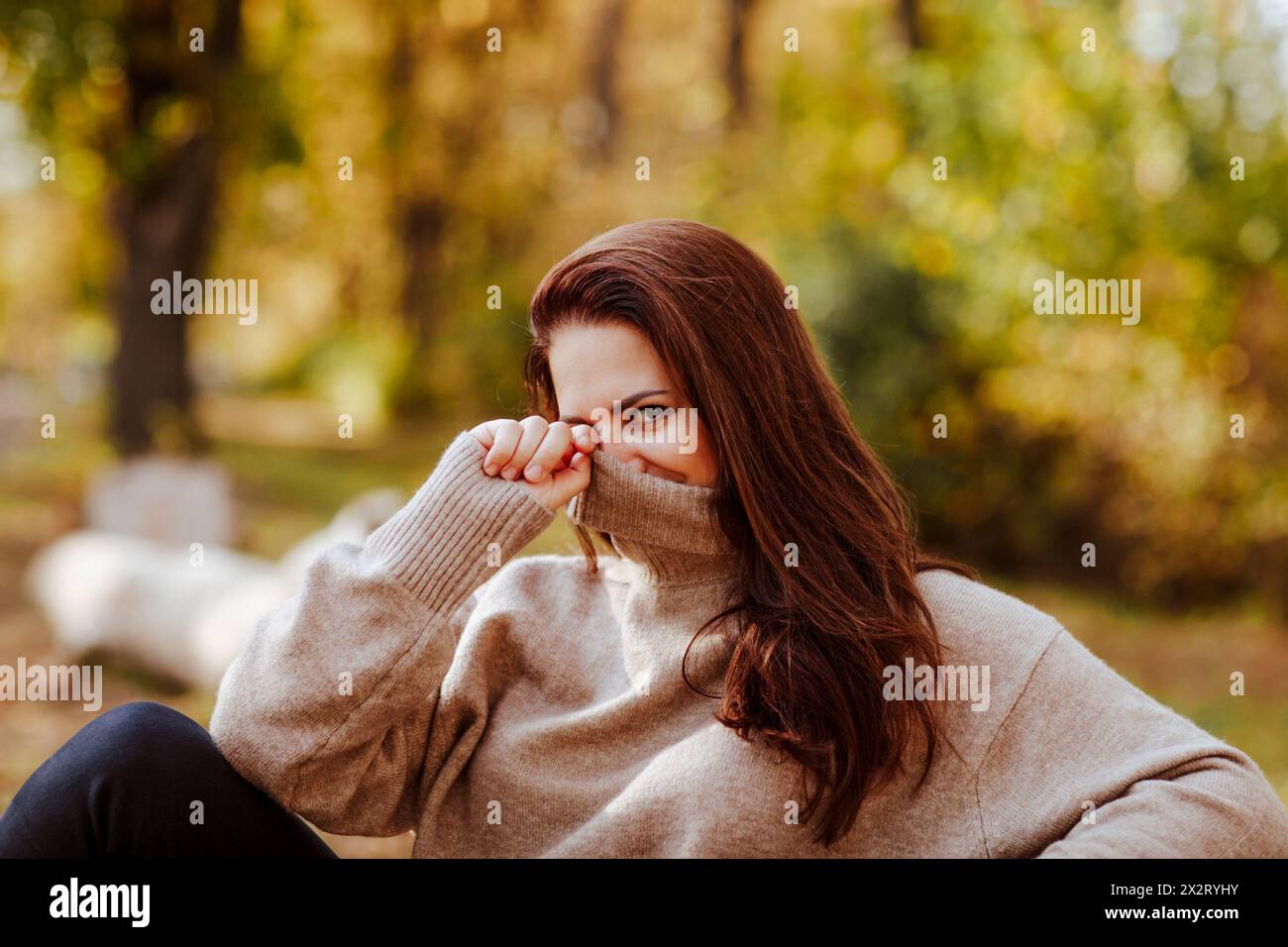 Reife Frau, die das Gesicht mit einem RollkragenT-Shirt im Park bedeckt Stockfoto