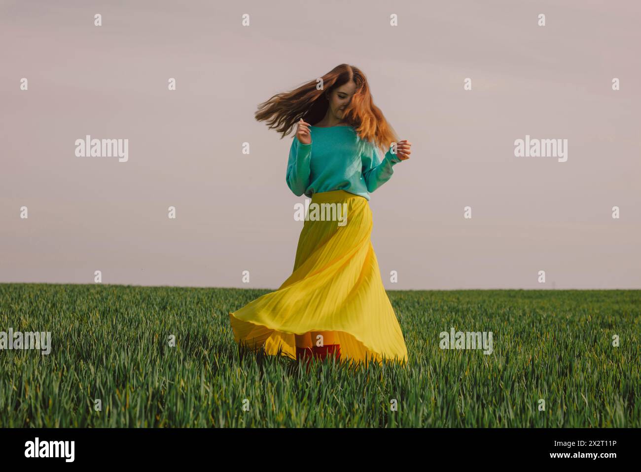 Glückliche Frau, die einen gelben Rock trägt und sich im grünen Weizenfeld dreht Stockfoto