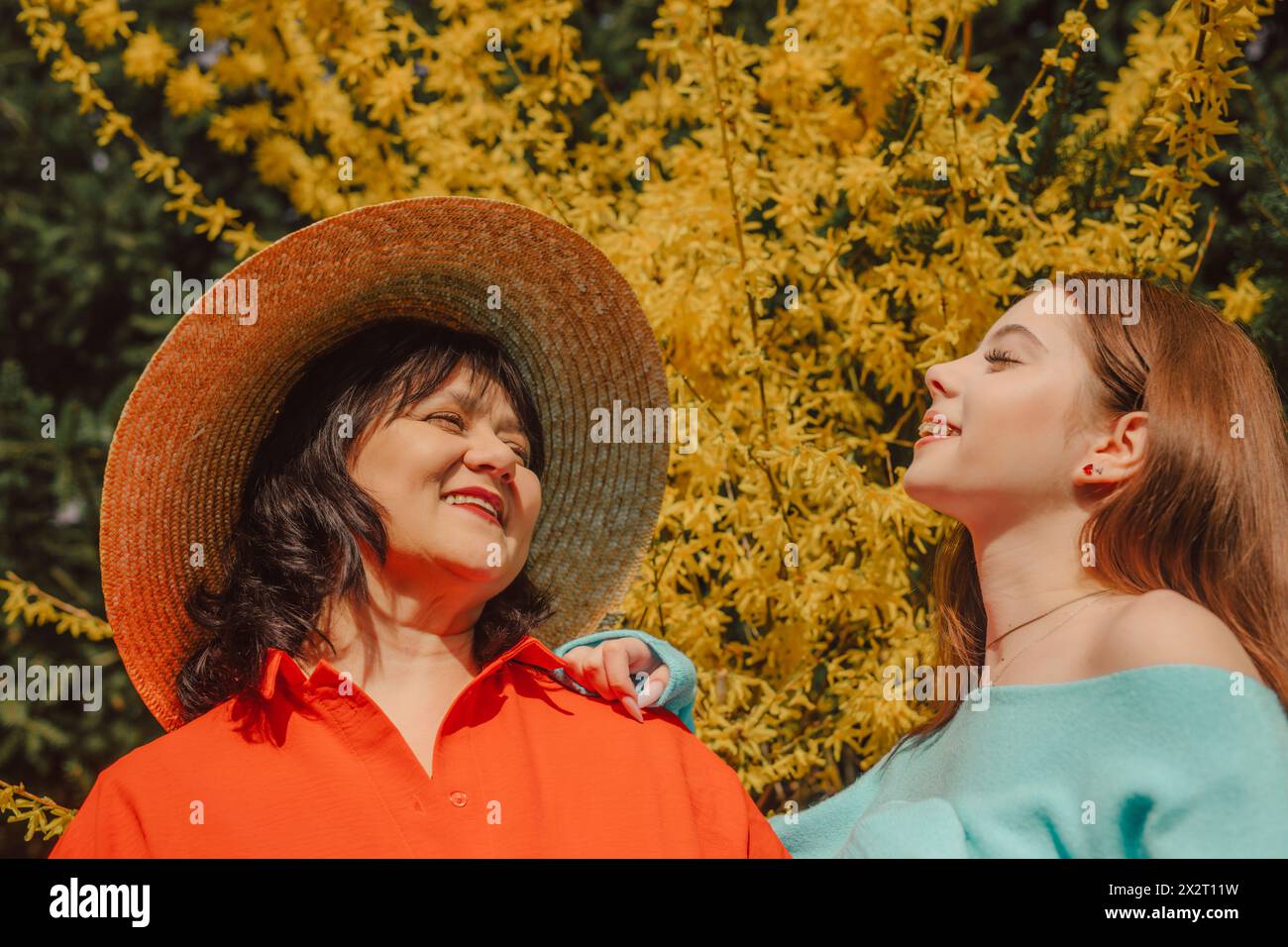 Glückliche Mutter und Tochter genießen Sonnenlicht in der Nähe des gelben Blütenbaums Stockfoto