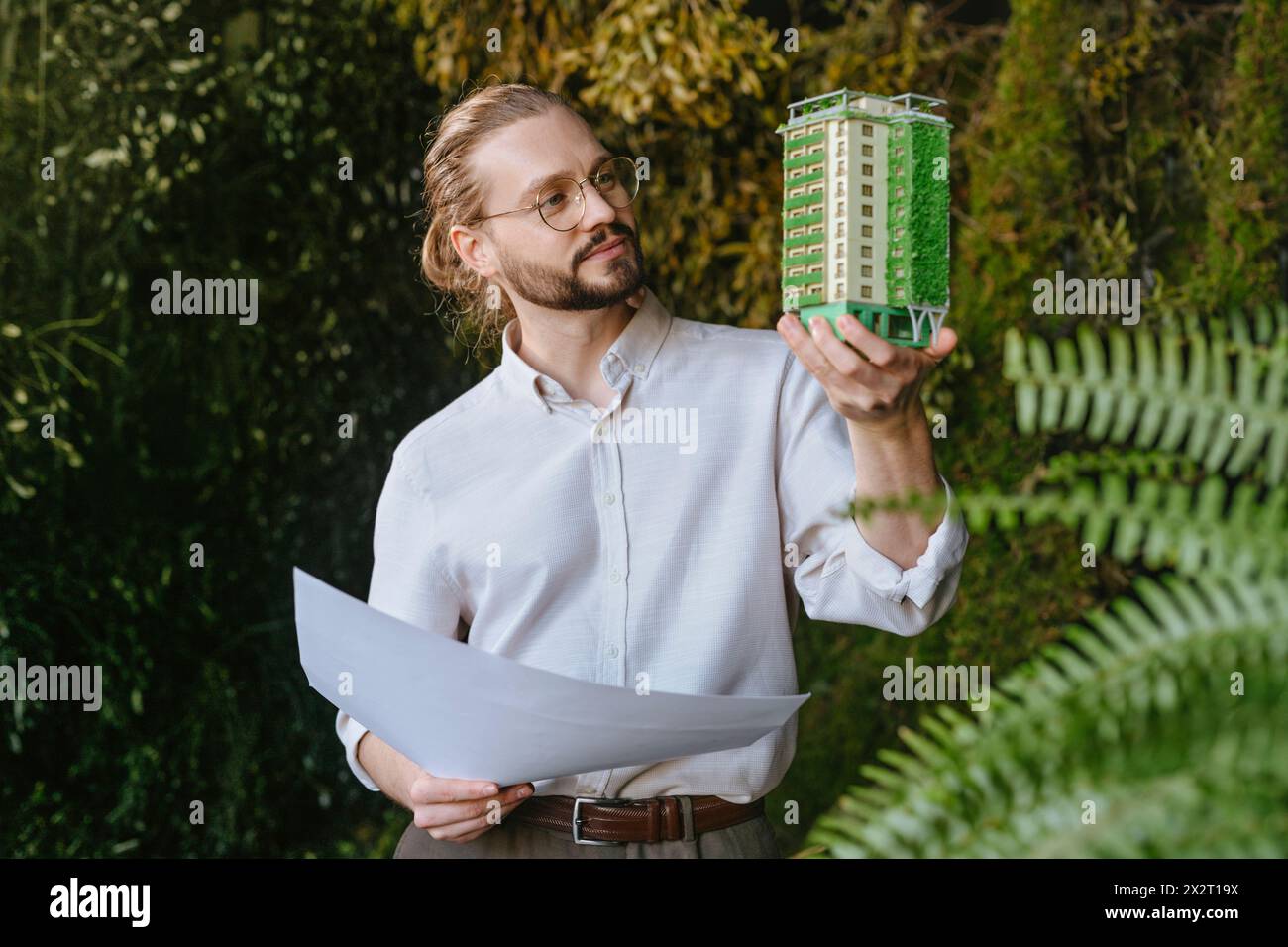 Architekt hält einen Plan und untersucht das Baumodell in der Nähe von Anlagen Stockfoto