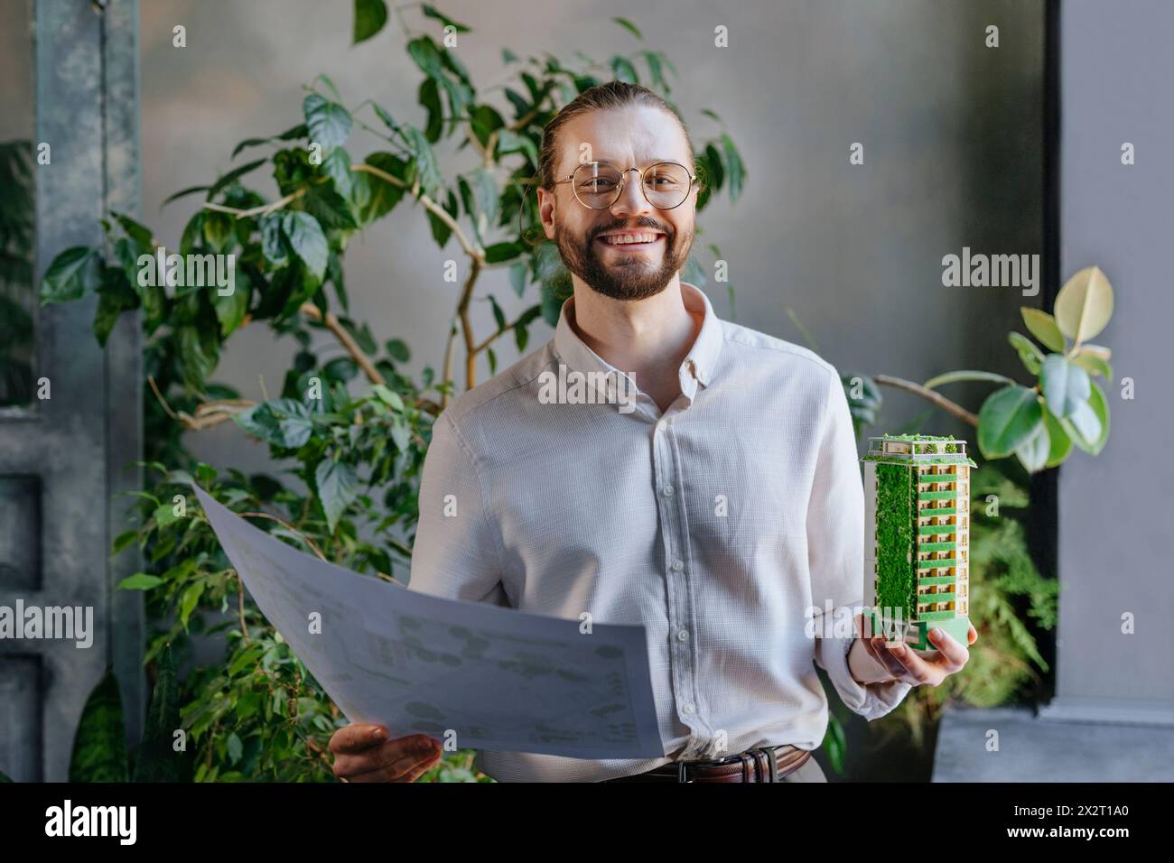 Glücklicher Architekt, der im Büro Pläne und Baumodelle hält Stockfoto