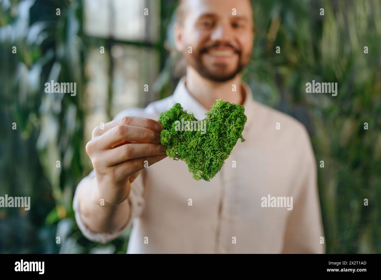 Lächelnder Geschäftsmann mit grünem, herzförmigem Moos Stockfoto