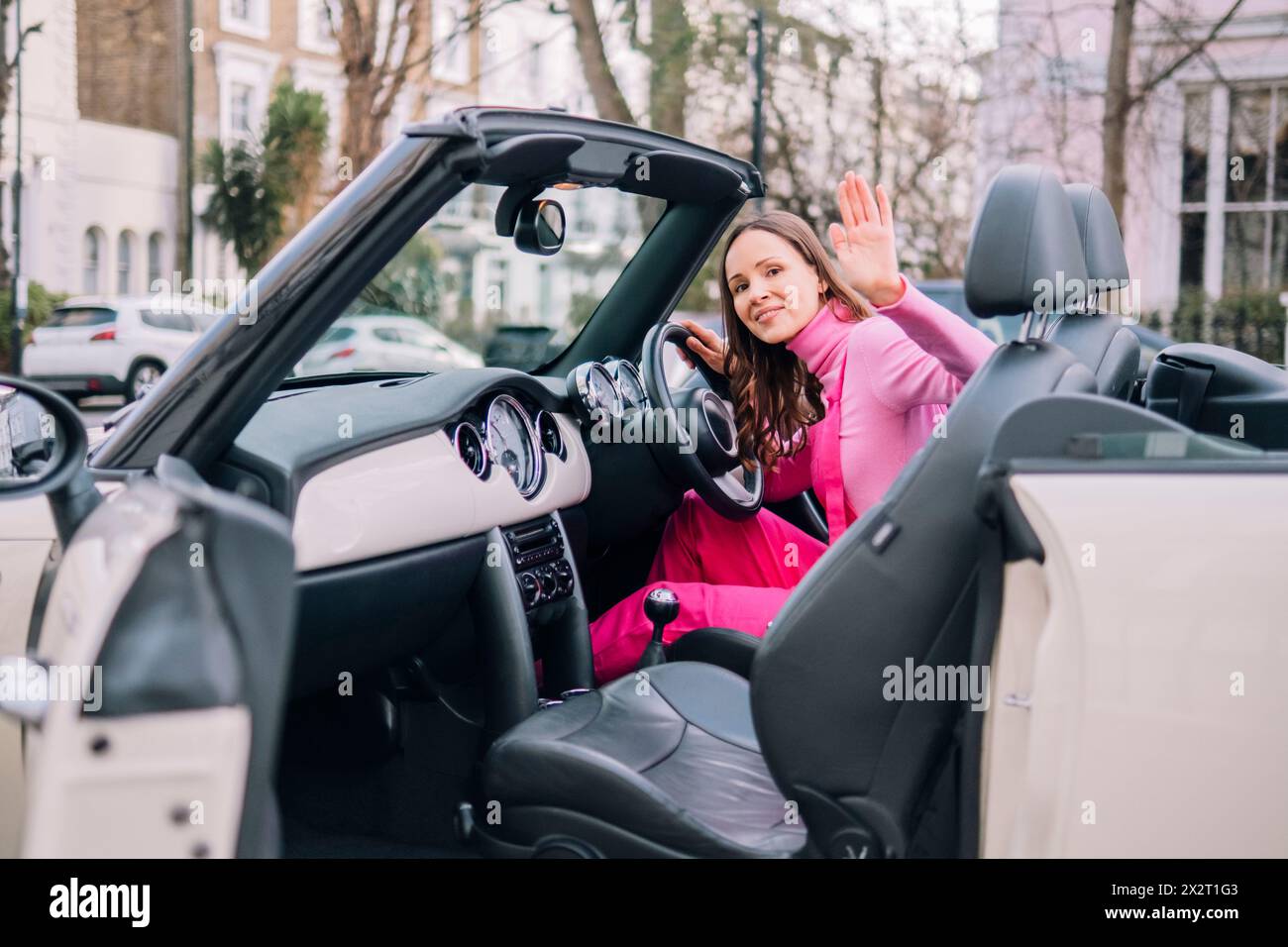 Lächelnde Frau, die im Cabrio sitzt und winkt Stockfoto