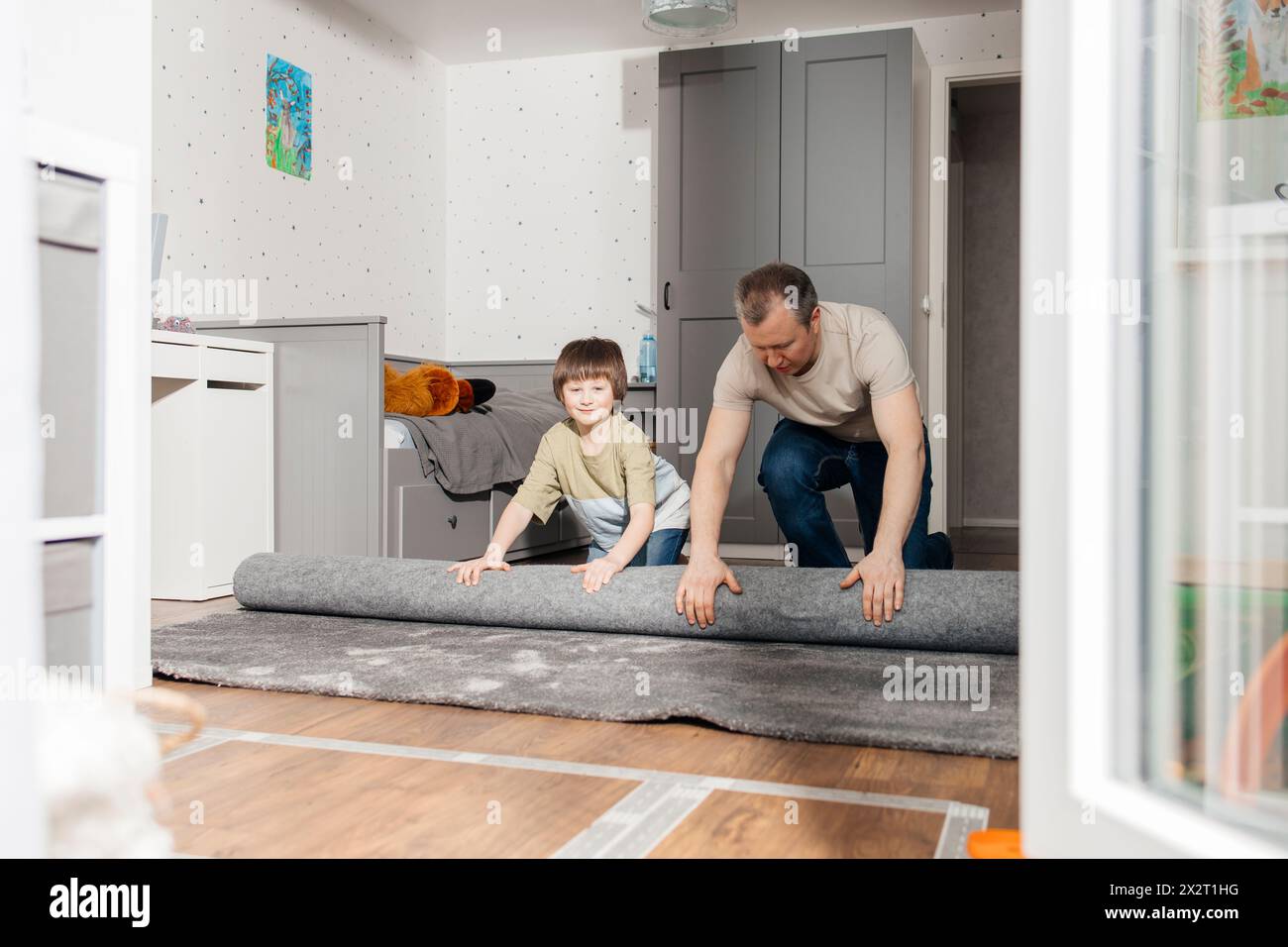 Junge, der Vater beim Ausrollen des Teppichs auf dem Boden zu Hause hilft Stockfoto
