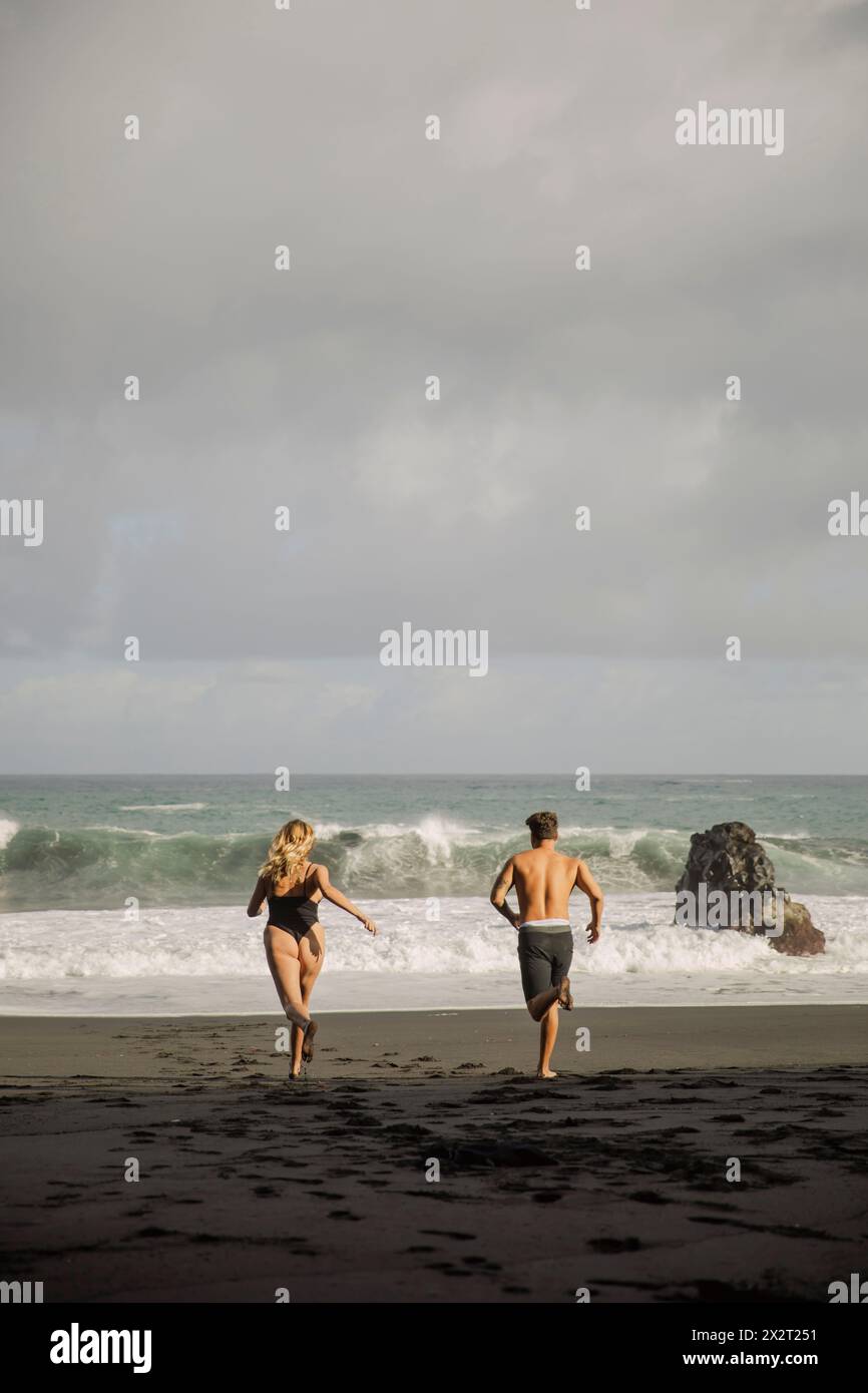Sorgloses junges Paar, das am Strand auf das Meer läuft Stockfoto Sorgloses junges Paar, das am Strand auf das Meer läuft Stockfoto