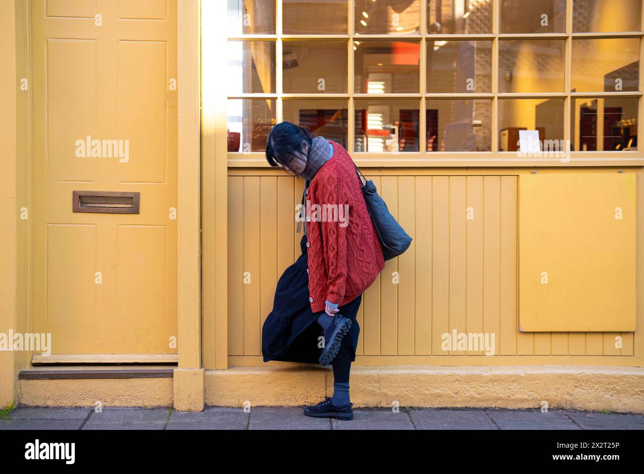 Frau, die Schuhe justiert, nahe dem gelben Gebäudeeingang Stockfoto