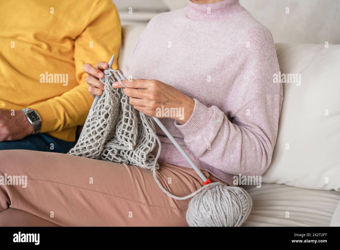 Hände einer Frau, die von einem Mann zu Hause auf dem Sofa strickt Stockfoto