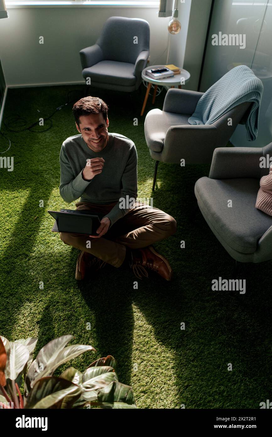 Glücklicher Geschäftsmann, der mit Tablet-PC auf grünem Teppich sitzt Stockfoto