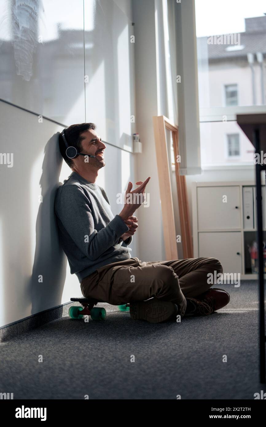 Fröhlicher Geschäftsmann, der über Headset spricht und im Büro Gesten macht Stockfoto