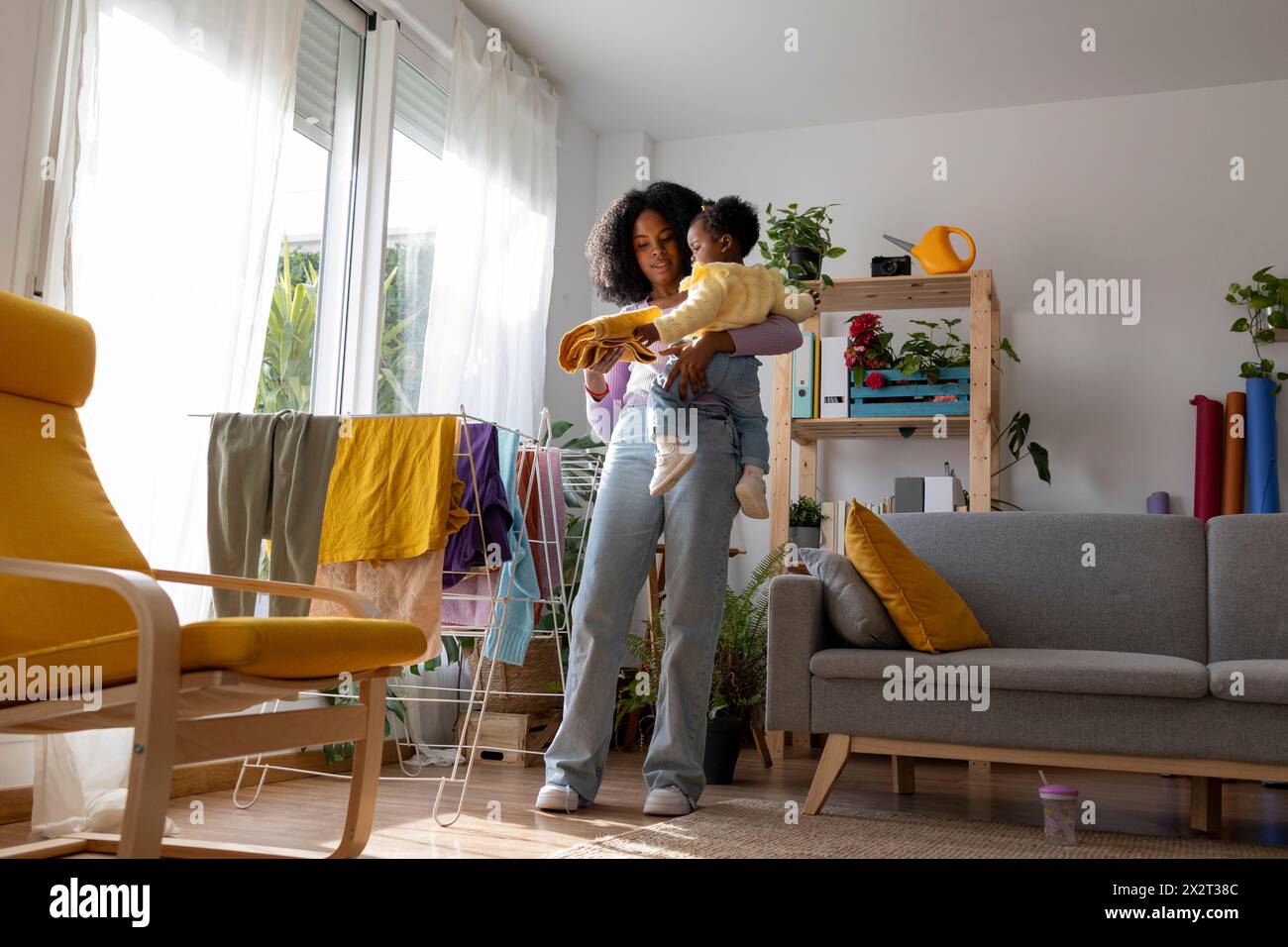 Junge alleinerziehende Mutter mit Tochter, die Kleidung im Wohnzimmer zu Hause trocknet Stockfoto