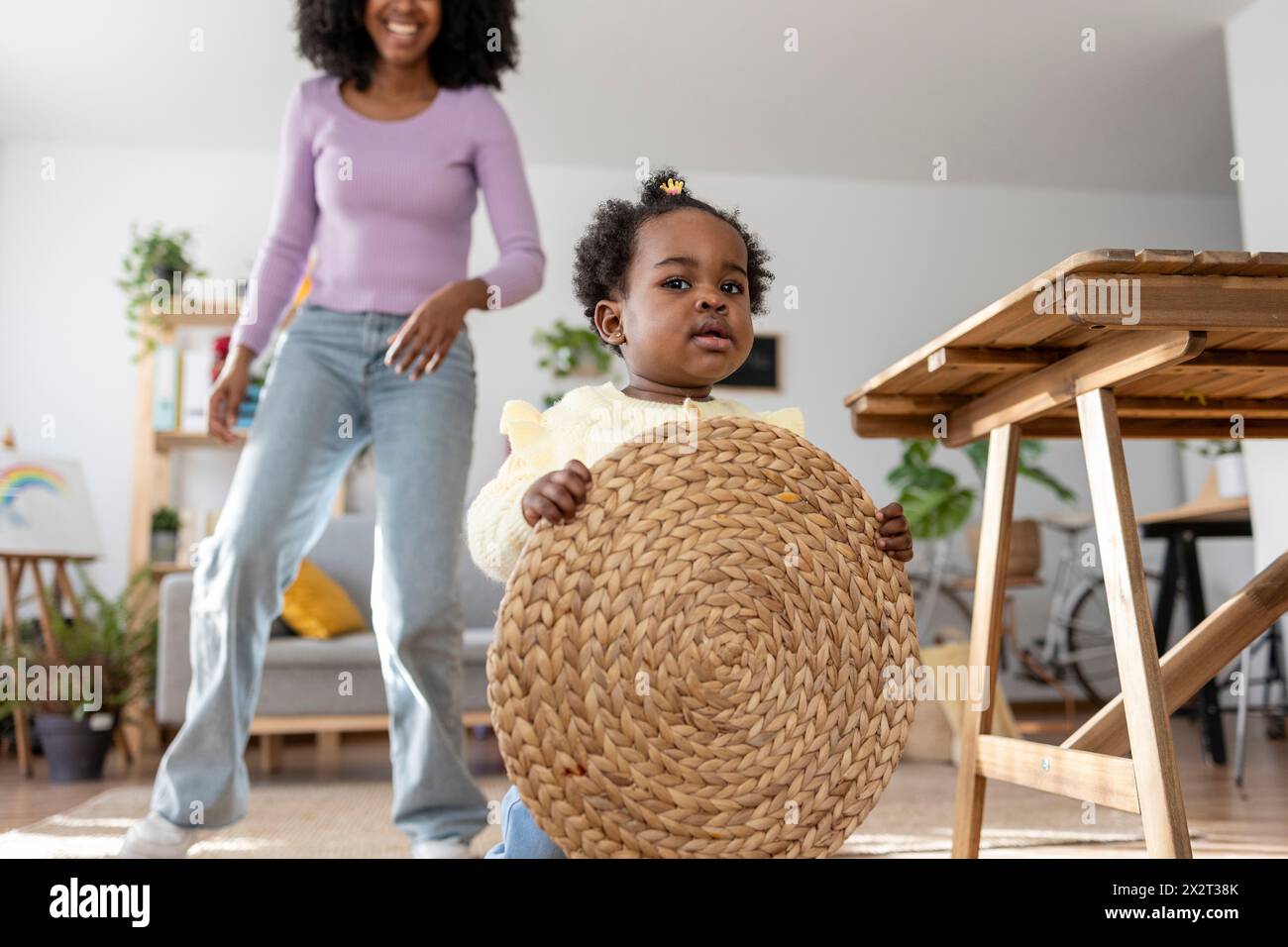 Niedliches Baby Mädchen mit kreisförmiger Platzmatte mit Mutter im Hintergrund zu Hause Stockfoto