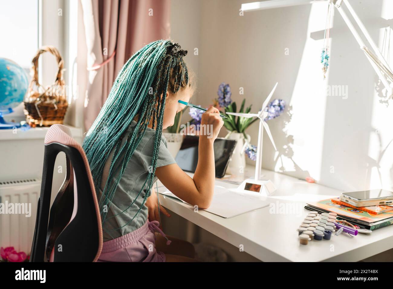 Mädchen mit gefärbten langen Haaren, das am Tisch von Windturbinenmodellen studiert Stockfoto