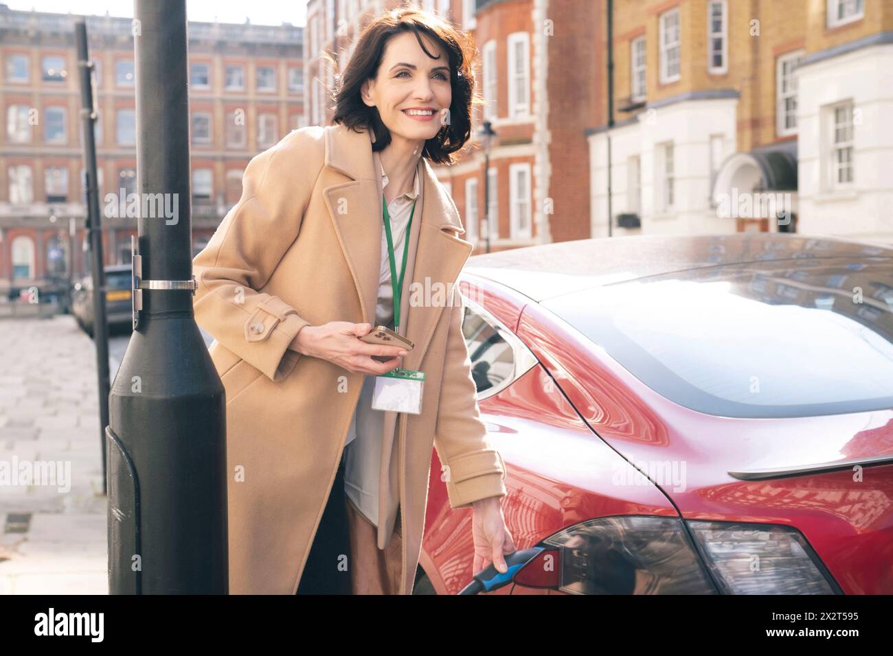 Lächelnde Geschäftsfrau, die Elektroauto in der Stadt auflädt Stockfoto