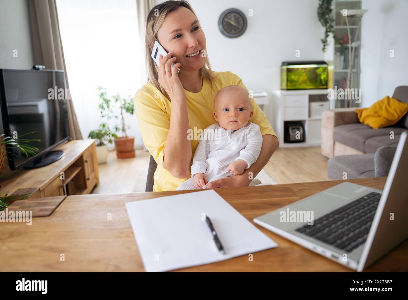Lächelnde Geschäftsfrau, die am Smartphone spricht und mit dem Sohn am Tisch sitzt Stockfoto