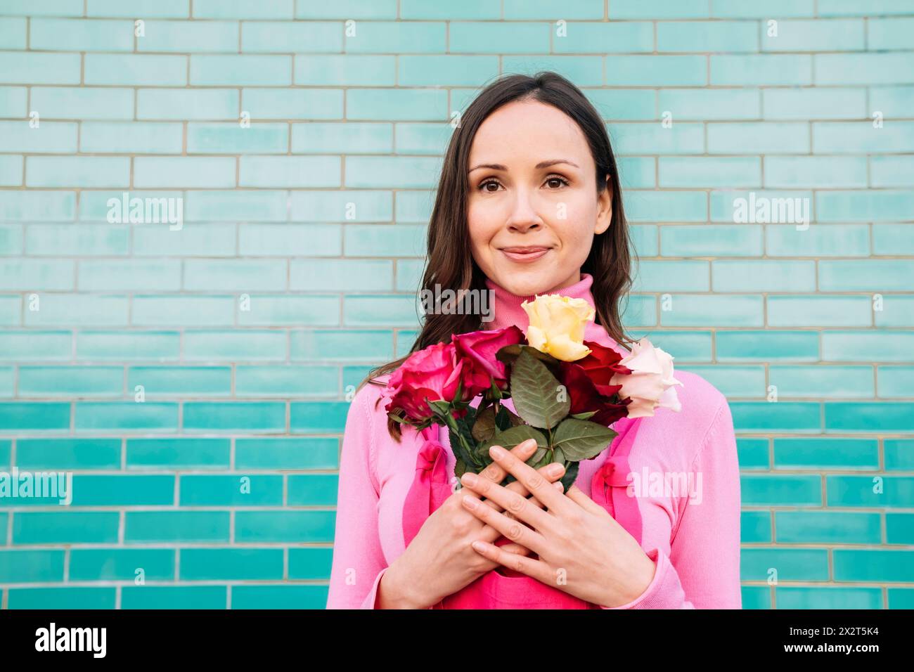 Lächelnde, schöne Frau mit Rosen vor der blauen Ziegelmauer Stockfoto