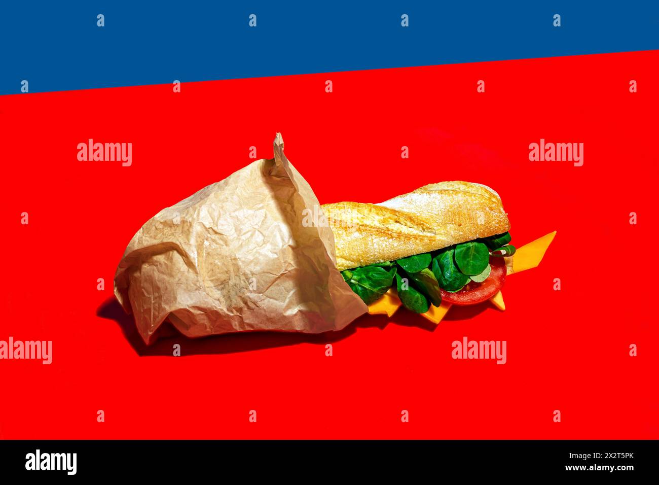 Sandwich mit frischem Käse und Gemüse in Papier auf rotem Hintergrund Stockfoto