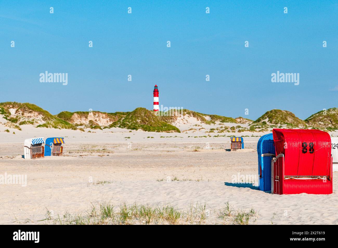 Deutschland, Schleswig-Holstein, Amrum, Sonnenliegen mit Kapuze am Sandstrand mit Leuchtturm im Hintergrund Stockfoto