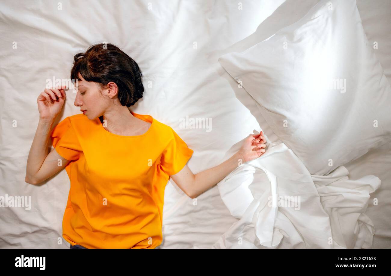Frau in gelbem T-Shirt, die zu Hause am Kissen auf dem Bett schläft Stockfoto