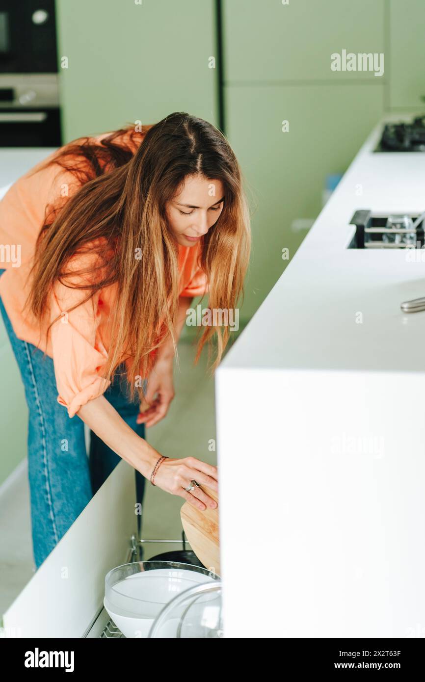 Frau mit langer Haarladeplatte im Geschirrspüler zu Hause Stockfoto