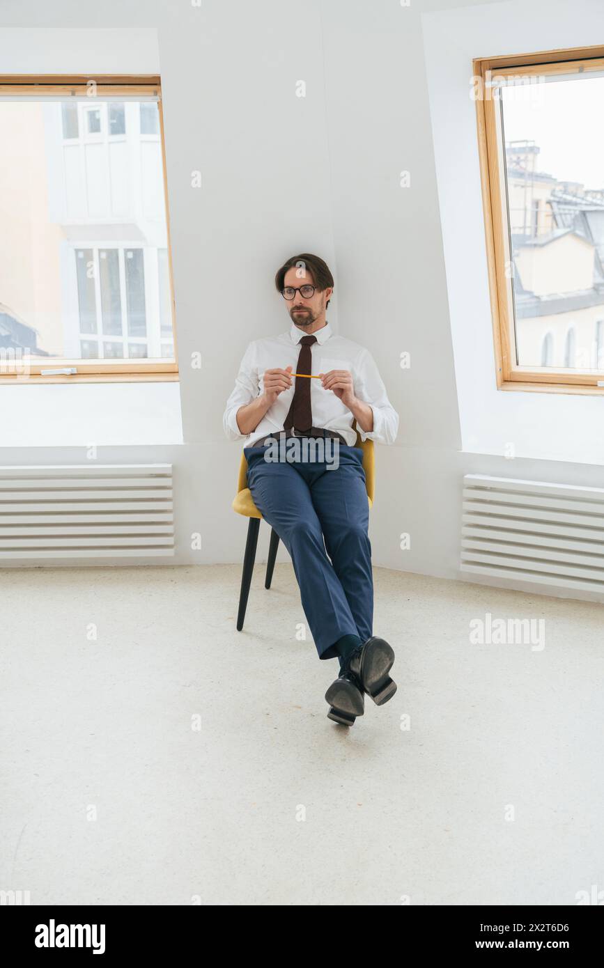 Geschäftsmann, der sich auf einem Stuhl zwischen Fenstern im Büro entspannt Stockfoto
