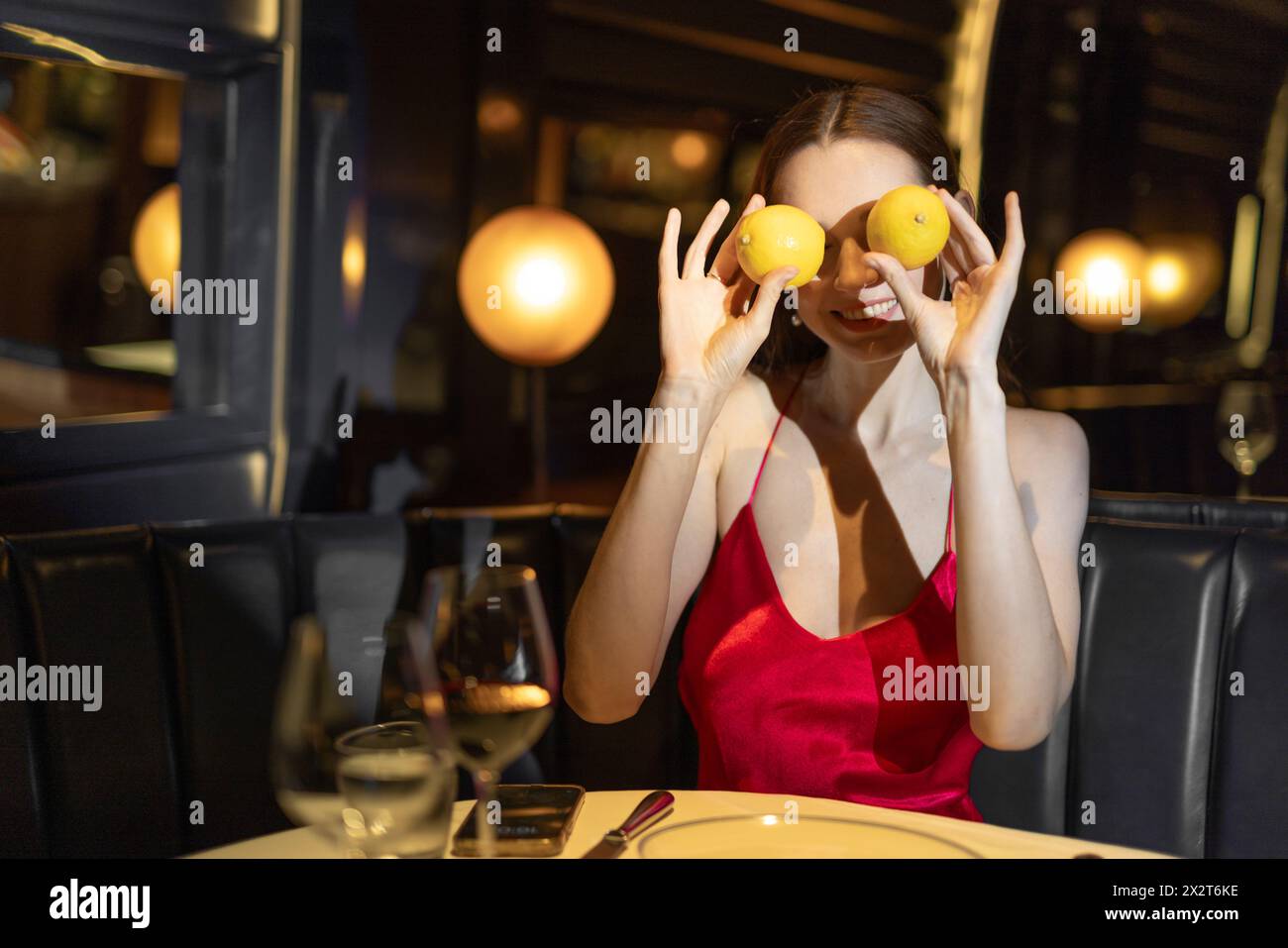Lächelnde Frau, die Augen mit Zitronen bedeckt, die im Restaurant sitzt Stockfoto