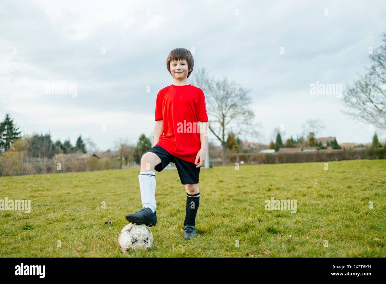 Lächelnder Junge, der mit Fuß auf Fußball auf dem Feld steht Stockfoto