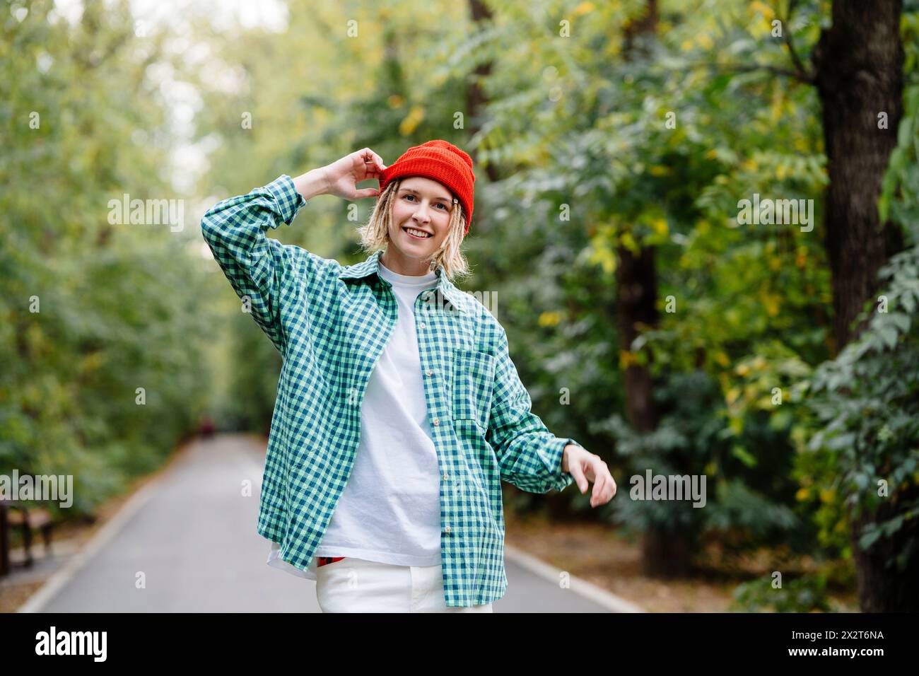 Lächelnde junge Frau mit Strickmütze und kariertem Hemd im Park Stockfoto