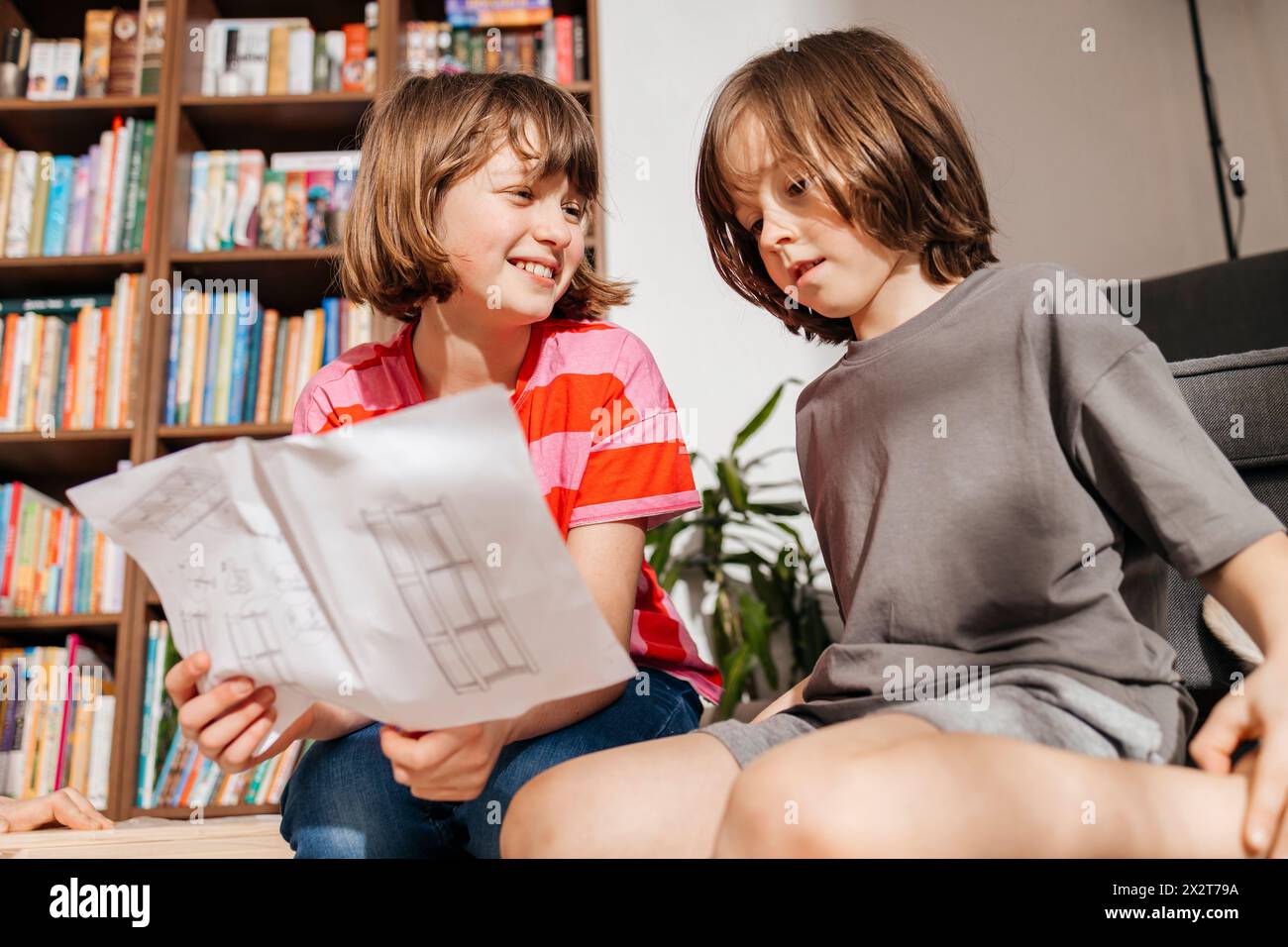 Lächelndes Mädchen mit Jungen, das Anweisungen für das Zusammenbauen von Möbeln zu Hause liest Stockfoto