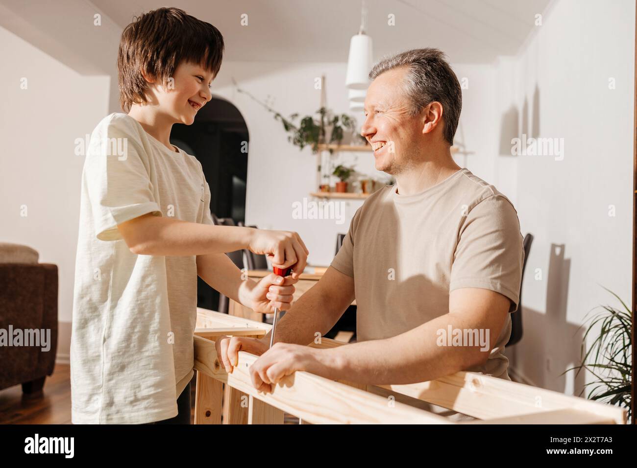 Glücklicher Sohn und Vater mit Schraubenzieher auf Holzmöbeln zu Hause Stockfoto