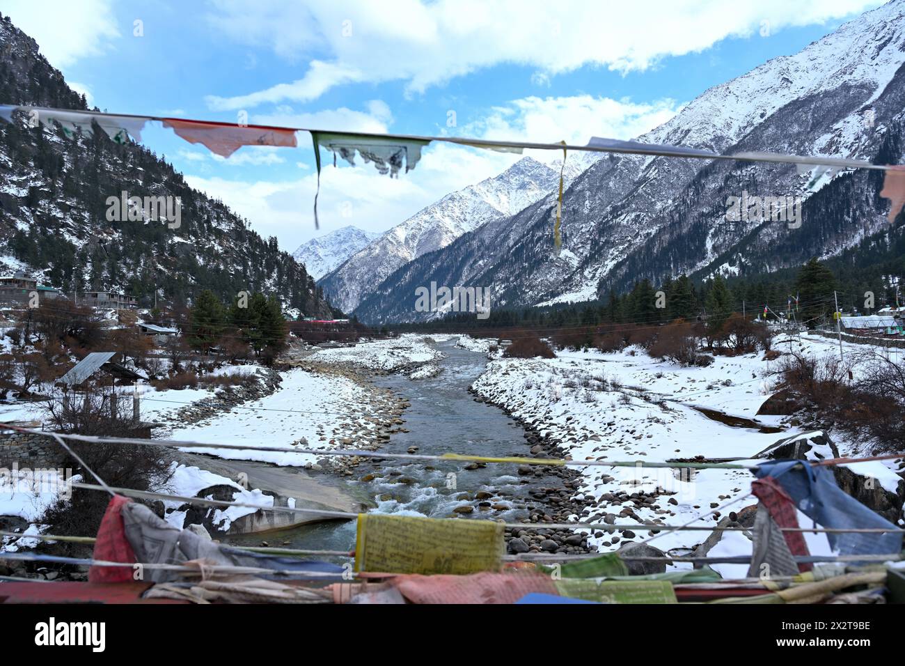 Der Baspa River fließt durch das schneebedeckte Tal, von der Brücke mit Gebetsfahnen aus gesehen, Rakcham, Himachal Pradesh, Indien, majestätische Himalaya-Berge. Stockfoto