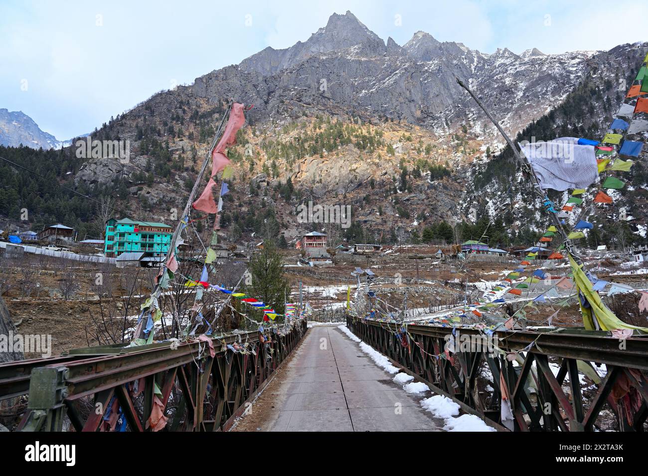 Eiserne Brücke mit bunten Gebetsfahnen im Dorf Rakcham, zerklüftete Himalaya-Berge im Hintergrund, Kinnaur, Himachal Pradesh, Indien. Stockfoto