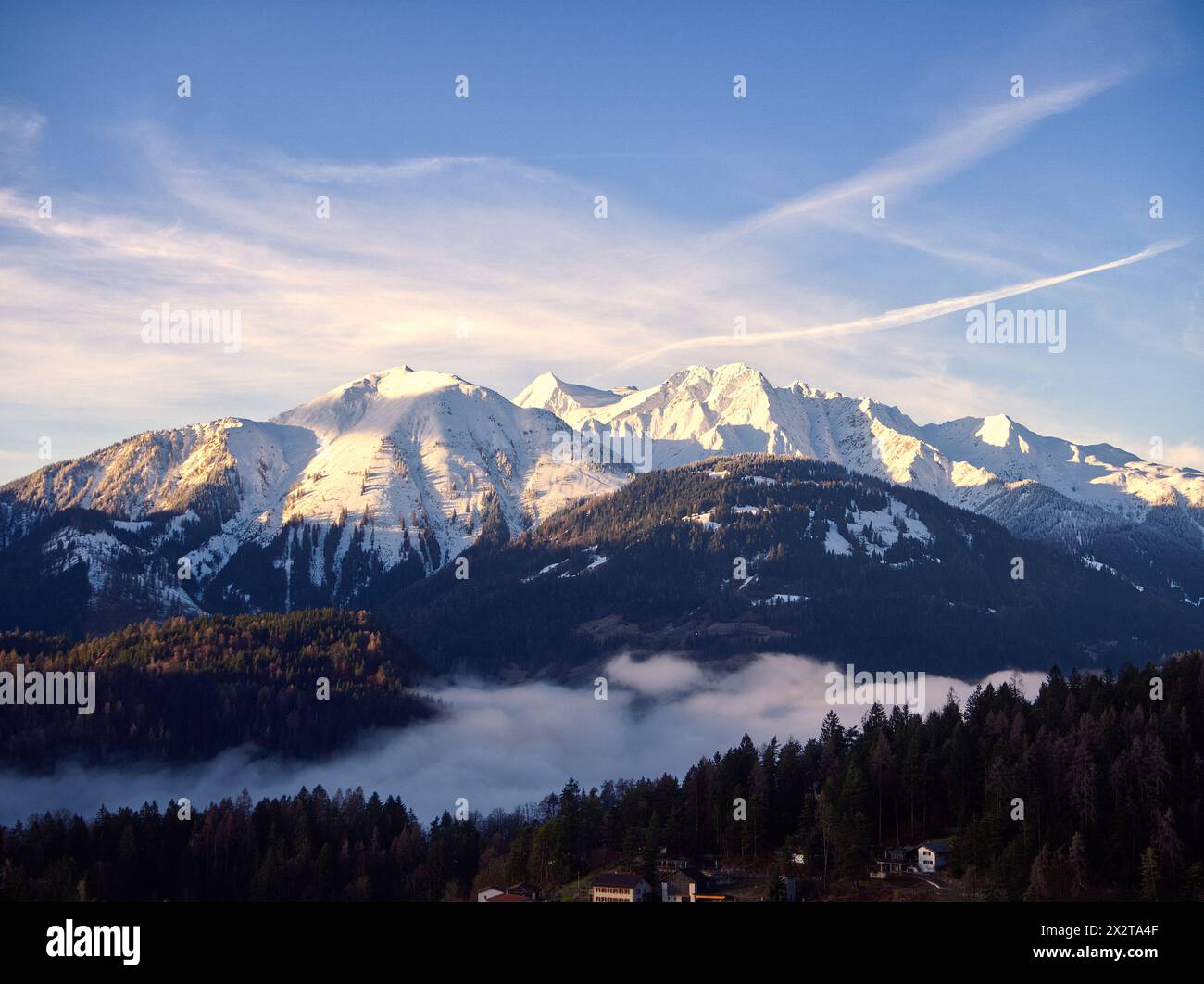 Alpenlandschaft mit schneebedecktem Bergblick mit niedrigen Wolken bei Sonnenaufgang in Laax, Schweiz. Die ersten Sonnenstrahlen am Horizont. Ruhige Stimmung. Stockfoto