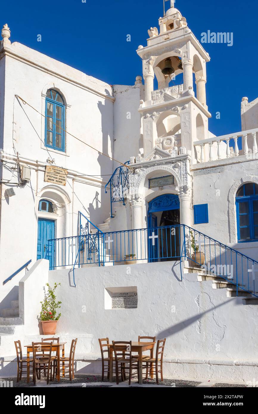 Der örtliche Platz des Dorfes Nikia, mit Holzstühlen eines nahegelegenen Kafenio, und die örtliche griechisch-orthodoxe Kirche der Marienpräsentation in Nisyros Stockfoto