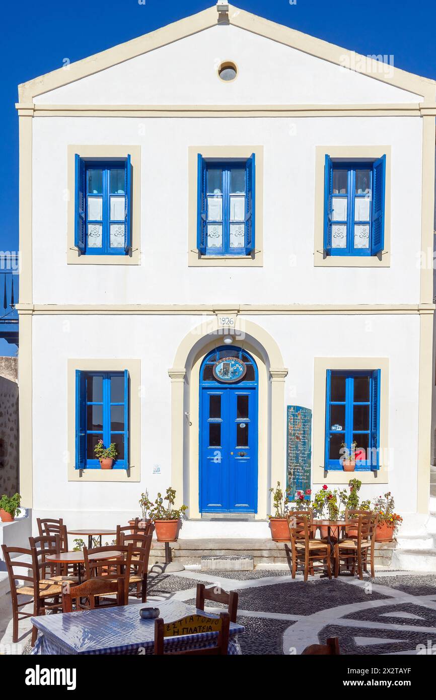 Der örtliche Platz des Dorfes Nikia, mit Holzstühlen eines nahegelegenen Kafenio, weiß getünchten Häusern und Kieselboden auf der Insel Nisyros, Griechenland, Europa. Stockfoto