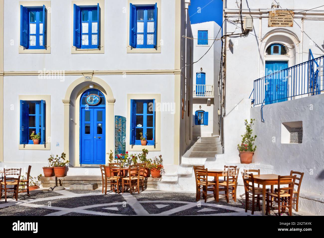 Der örtliche Platz des Dorfes Nikia, mit Holzstühlen eines nahegelegenen Kafenio, weiß getünchten Häusern und Kieselboden auf der Insel Nisyros, Griechenland, Europa. Stockfoto