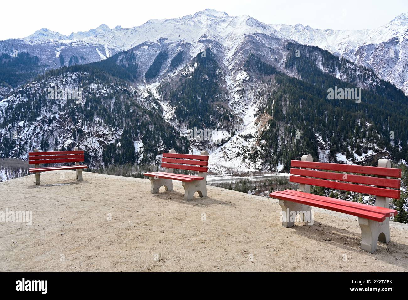 Zementierte Bänke mit roten Rückenlehnen mit Blick auf die Berge des Sangla Valley, Himachal Pradesh, Indien. Friedliche Außenlandschaft mit Schnee und Wald. Stockfoto