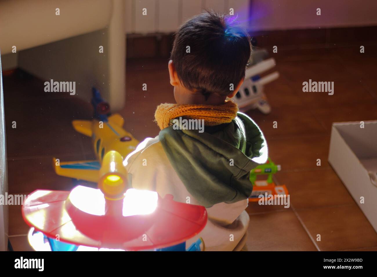 Kinderwundern: Kleines Kind umgeben von Spielzeugen, gebadet in farbenfrohen Kameraflampen. Erleben Sie den Zauber der Kindheit als kleines Kind. Stockfoto