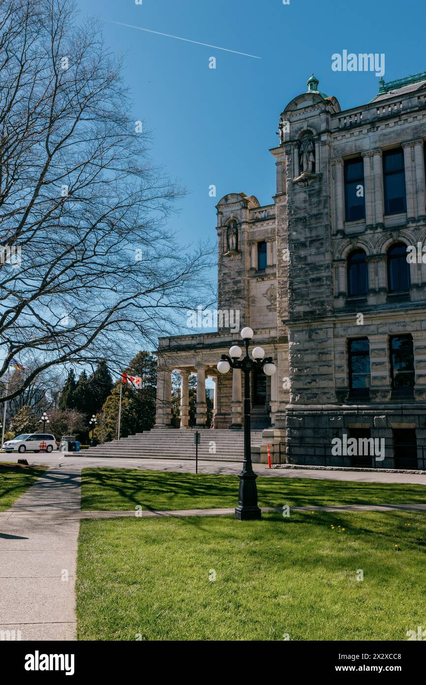 Ein Blick auf die südöstliche Seite des Gebäudes der Legislative Assembly of BC gegenüber einem blattlosen Baum mit einem blauen wolkenlosen Himmel im Hintergrund Stockfoto