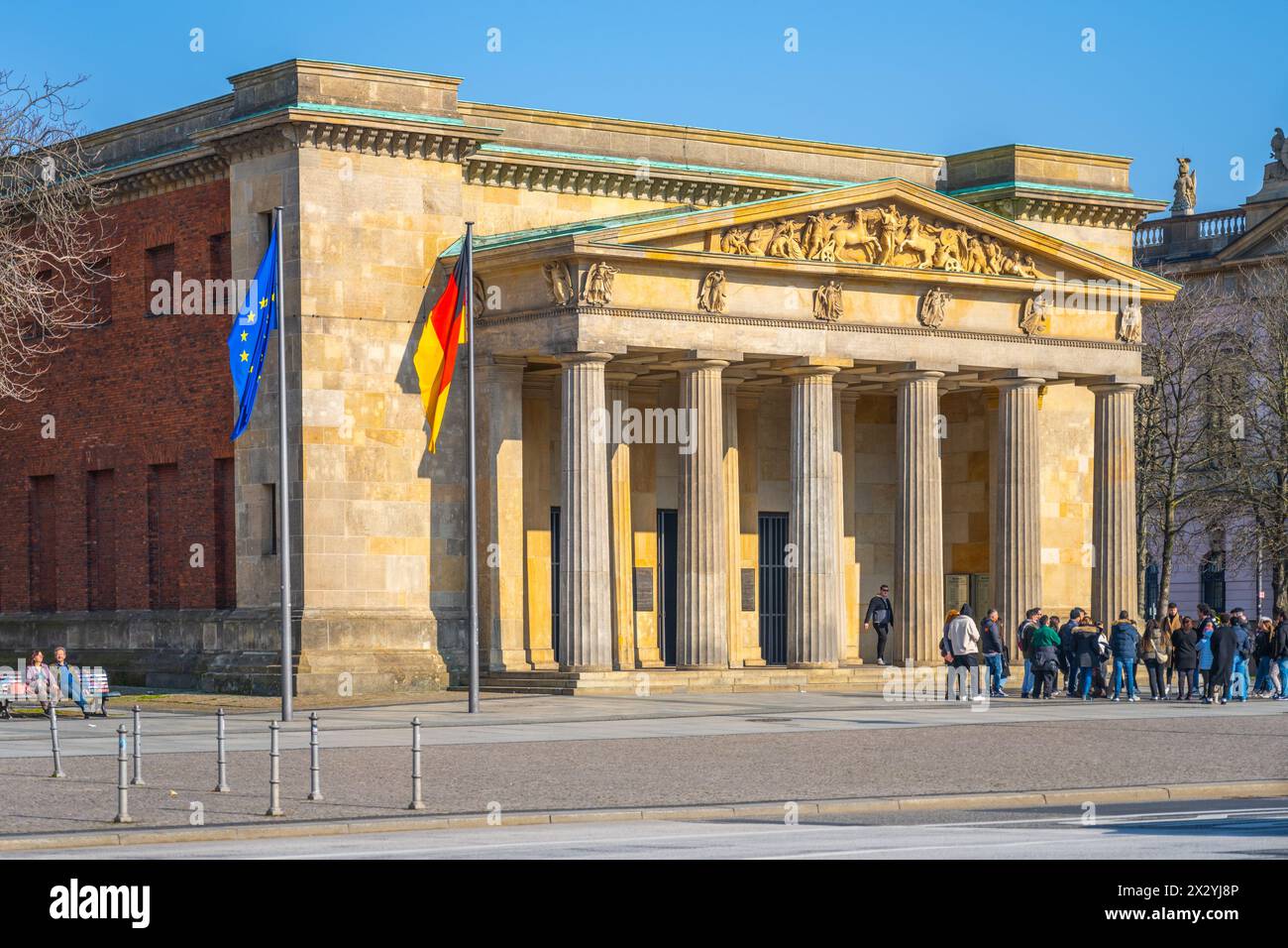 Die neue Wache (englisch: New Watchhouse), ein historisches Gebäude in Berlin, steht unter klarem Himmel, mit Besuchern am Eingang. Stockfoto