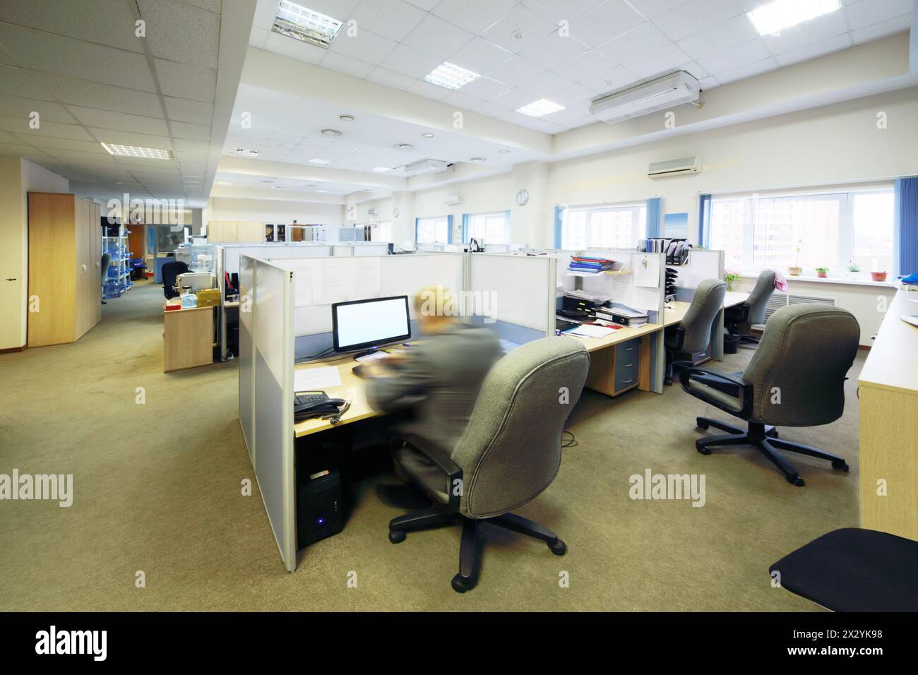 Die Leute sitzen in einem großen, hellen Büro mit getrennten Arbeitsplätzen. Stockfoto